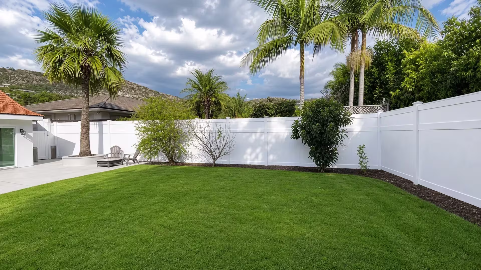 White vinyl privacy fence turns a corner behind a large shrub near patio chairs and lawn contours