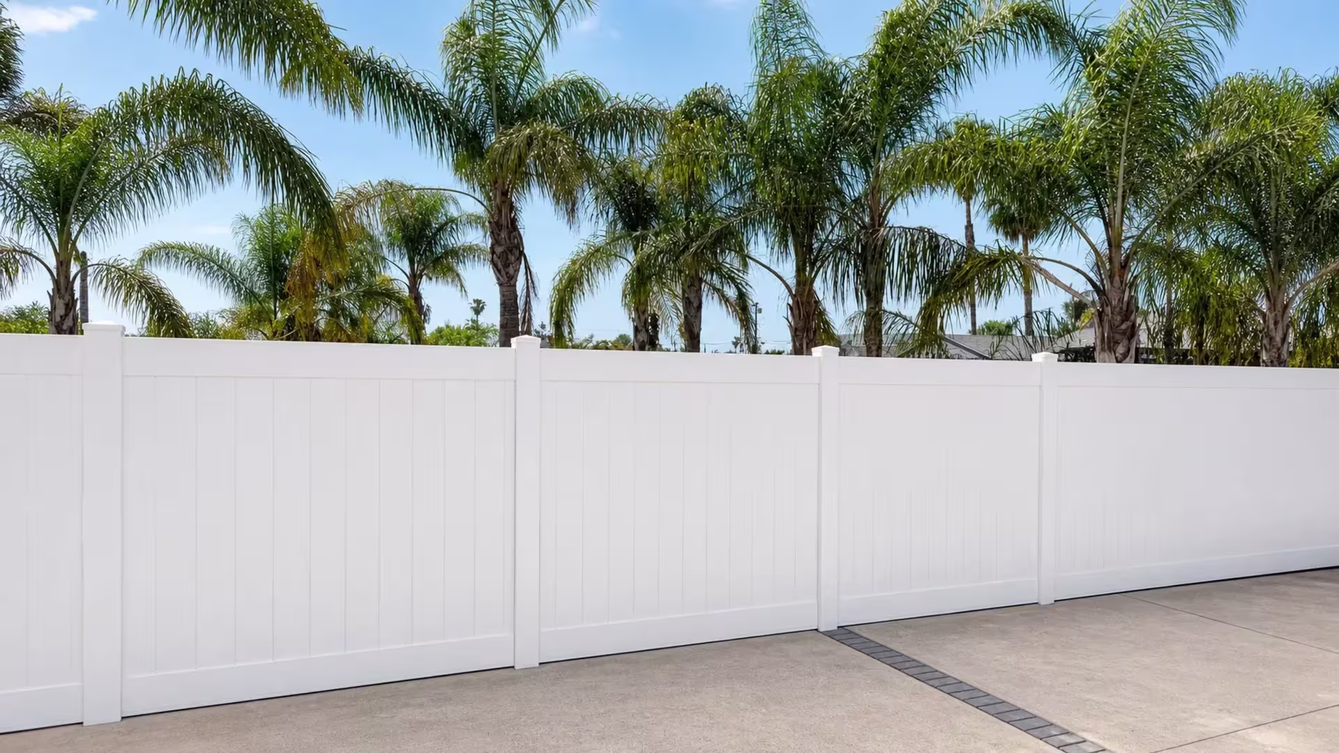 White vinyl vertical privacy fence runs continuously past palm trees with no gate or opening