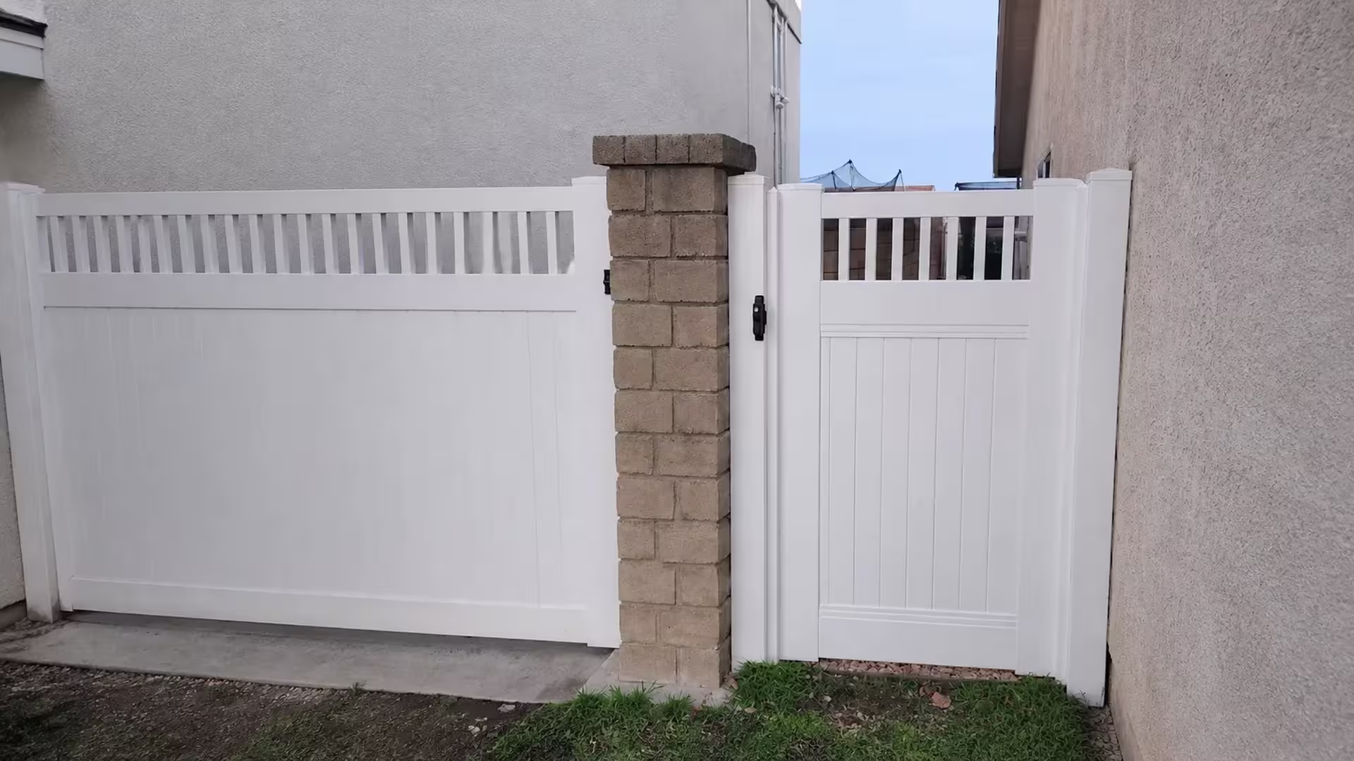 A narrow stucco passage frames the White vinyl single gate topped with vertical pickets on this Santa Clarita property