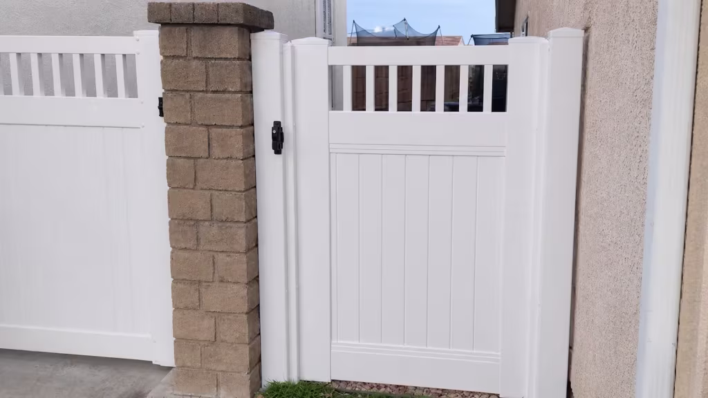 Through the vertical picket top, a distant rooftop shows past this White vinyl single gate set in a stucco passage