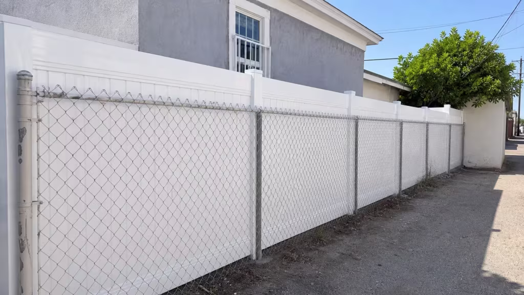 This solid White vinyl fence adds privacy behind the existing chain-link along a paved rear alley in Lincoln Heights