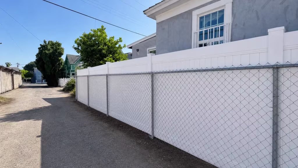 A barred multi-pane window overlooks this White vinyl privacy fence running along the alley in Lincoln Heights