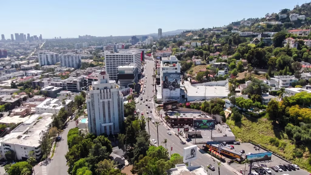 High-rises crowd a dense urban corridor in West Hollywood, with downtown's skyline visible far in the distance