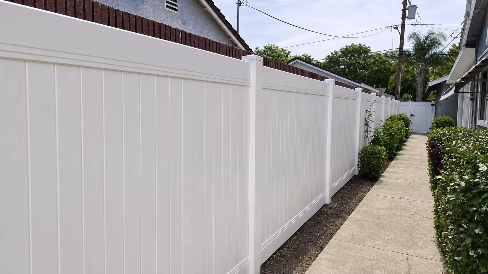 A Long Beach walkway runs beside a brick-topped masonry wall, with this White vinyl privacy fence keeping a level top line