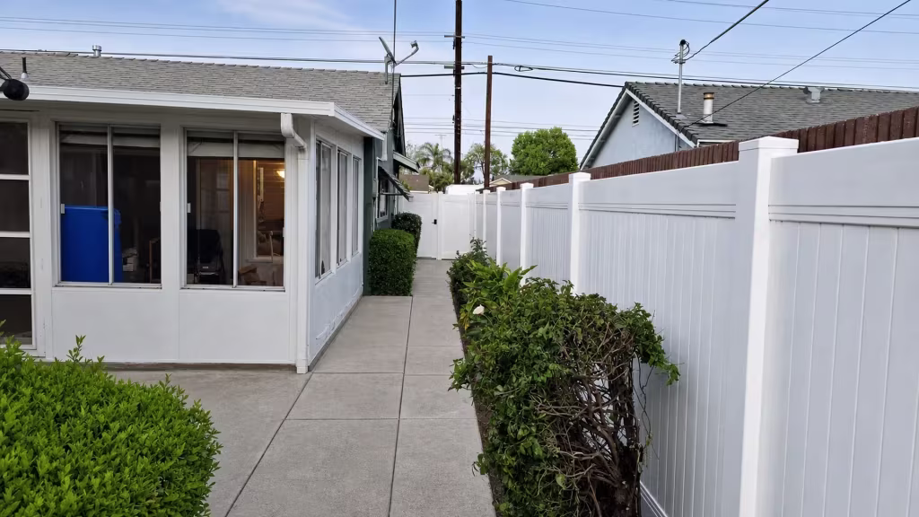 Overhead wires and antennas cross above a Long Beach planting strip where this White vinyl privacy fence closes the side yard