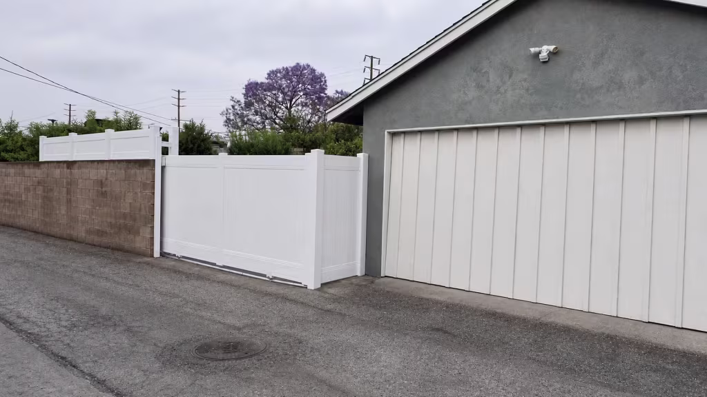 A paved alley runs behind this White vinyl privacy fence and matching gate along a masonry boundary in Long Beach