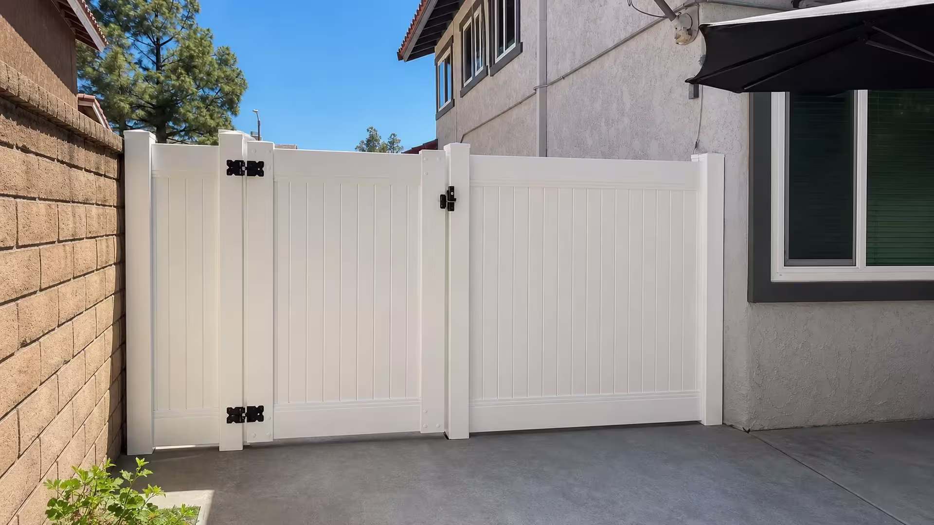 A satellite dish and exterior conduit mark the stucco house wall in Simi Valley, beside this White vinyl fence and gate