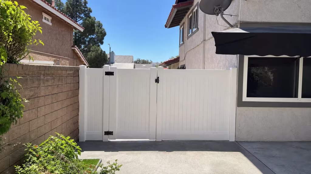 Unequal White vinyl gate leaves close this Simi Valley fence line between a tan masonry wall and the stucco house