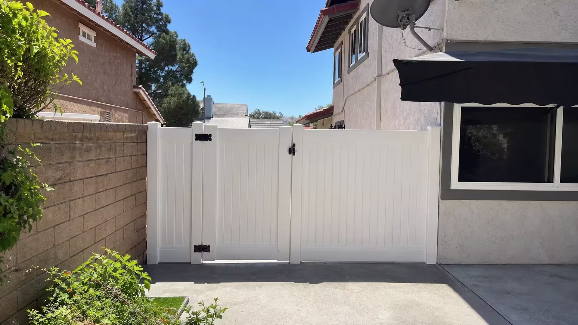 Unequal White vinyl gate leaves close this Simi Valley fence line between a tan masonry wall and the stucco house