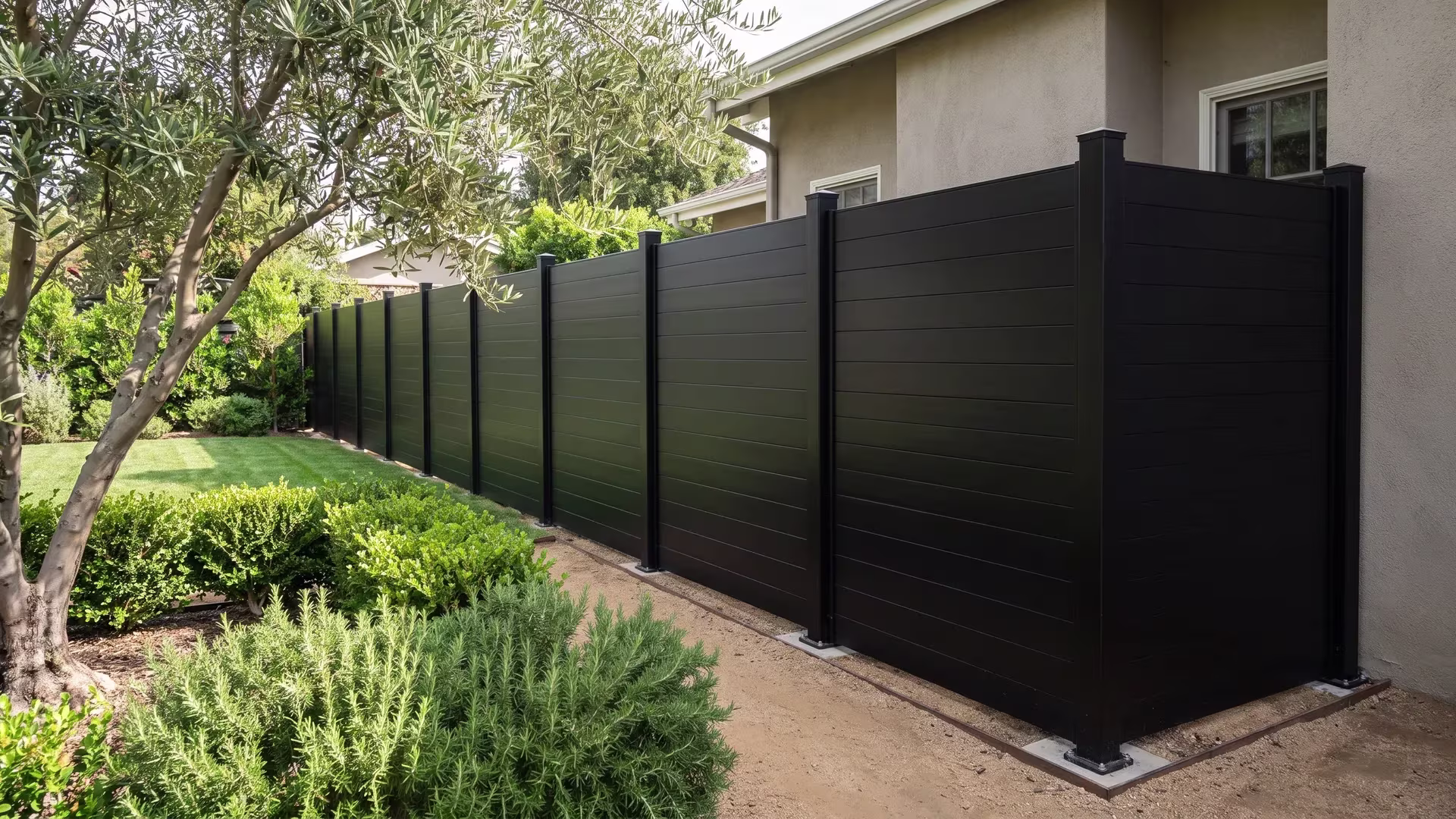 Mature olive trees front a Black aluminum privacy fence that ends flush against the house wall