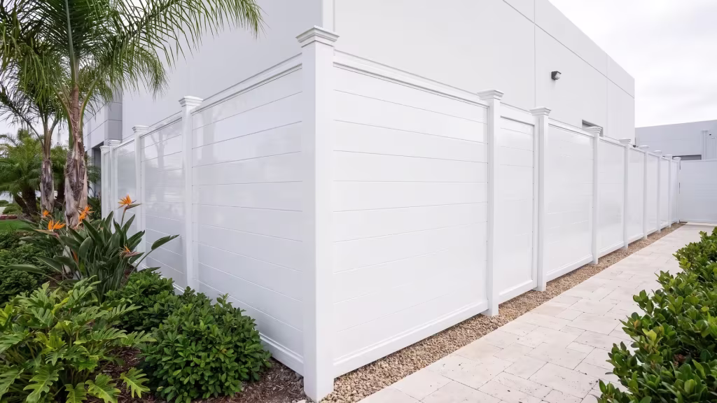 White aluminum privacy fence continuing behind layered planting beside a gravel maintenance band