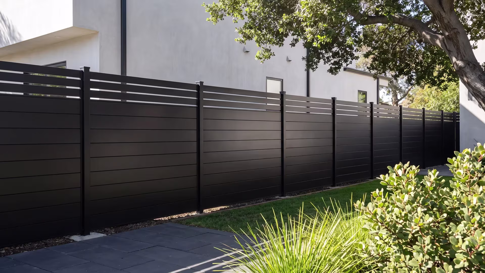 A Black aluminum privacy fence encloses this courtyard, its picket top framing a minimalist stucco home