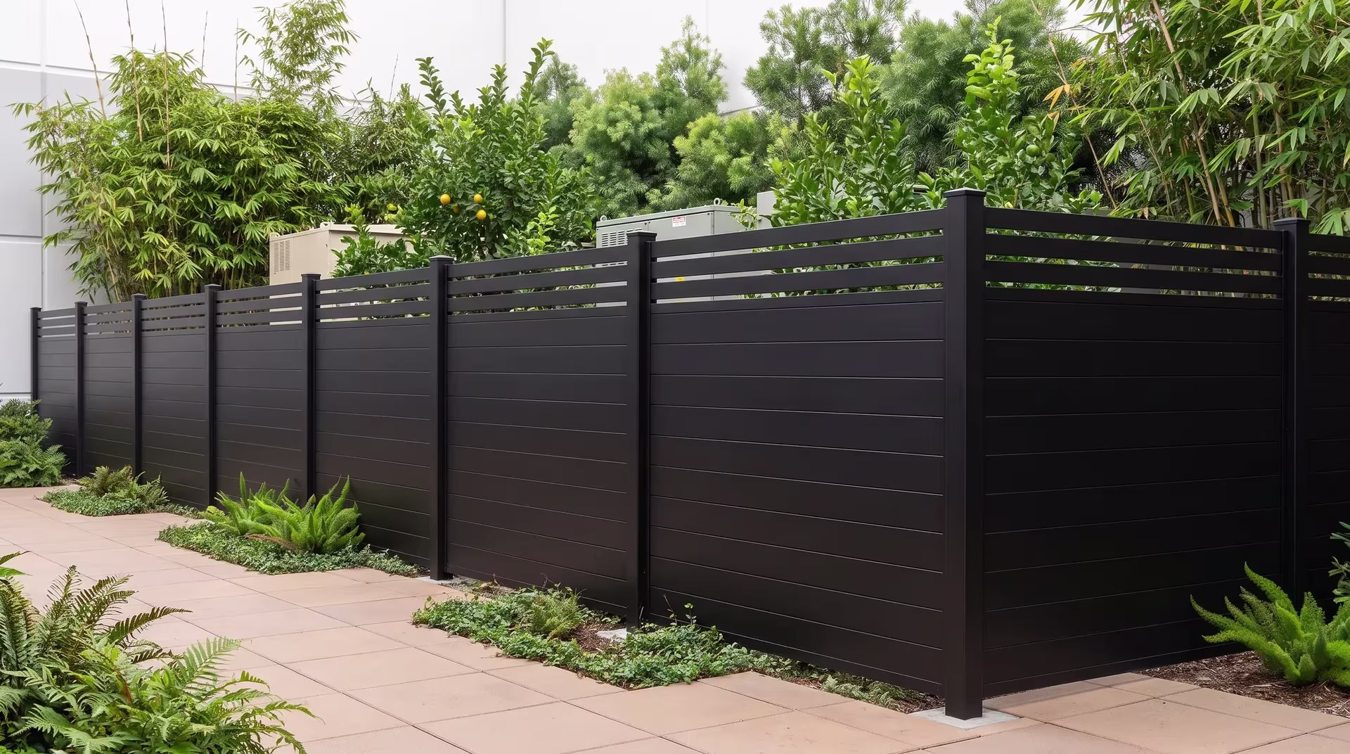 Dense fern and bamboo screening border this Black aluminum privacy fence along warm architectural paving