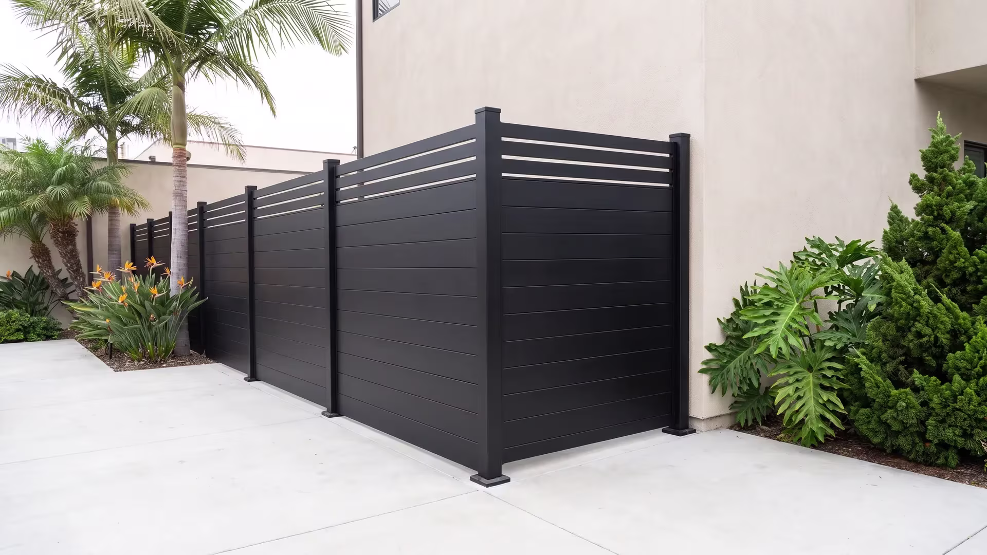 A Black aluminum privacy fence ends flush against a stucco courtyard wall near queen palms