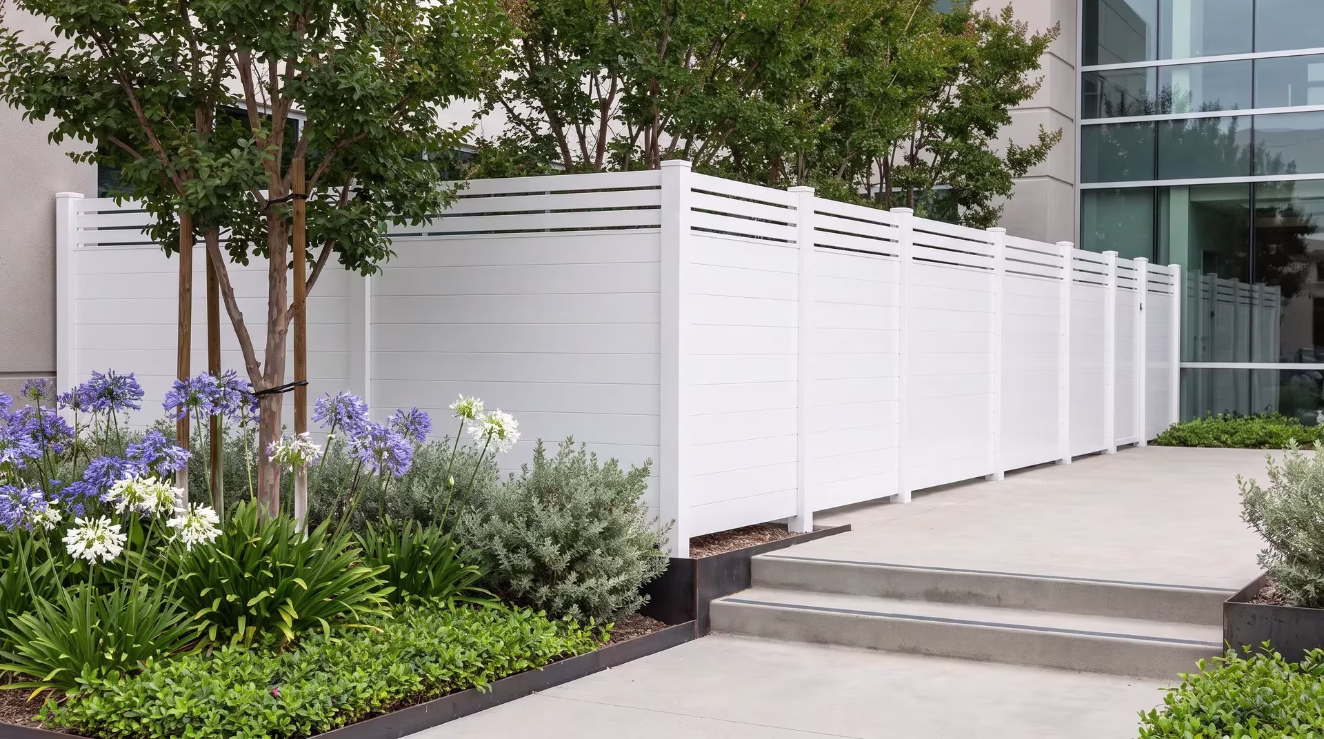 A glass-and-stucco office building borders this White aluminum privacy fence beside a landscaped break courtyard