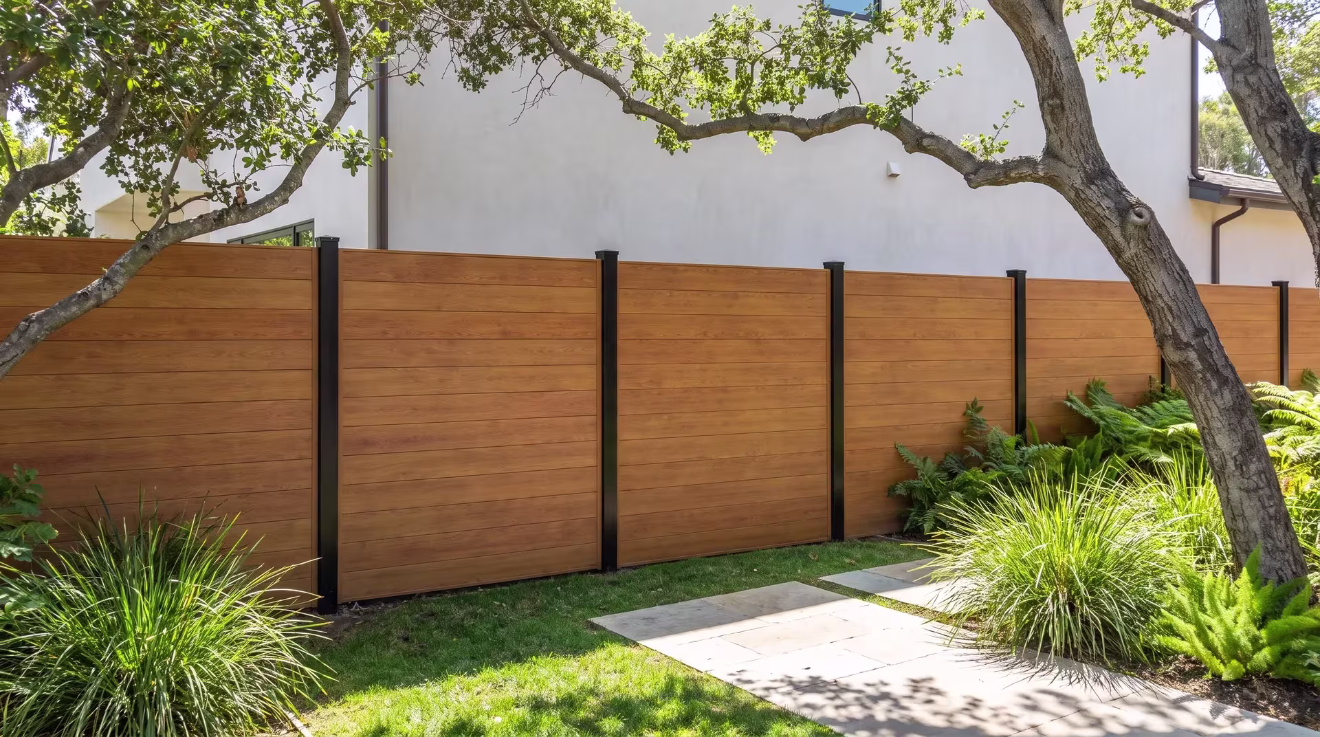 Ferns and lomandra line this Woodgrain aluminum privacy fence holding a level run past a stucco backyard facade