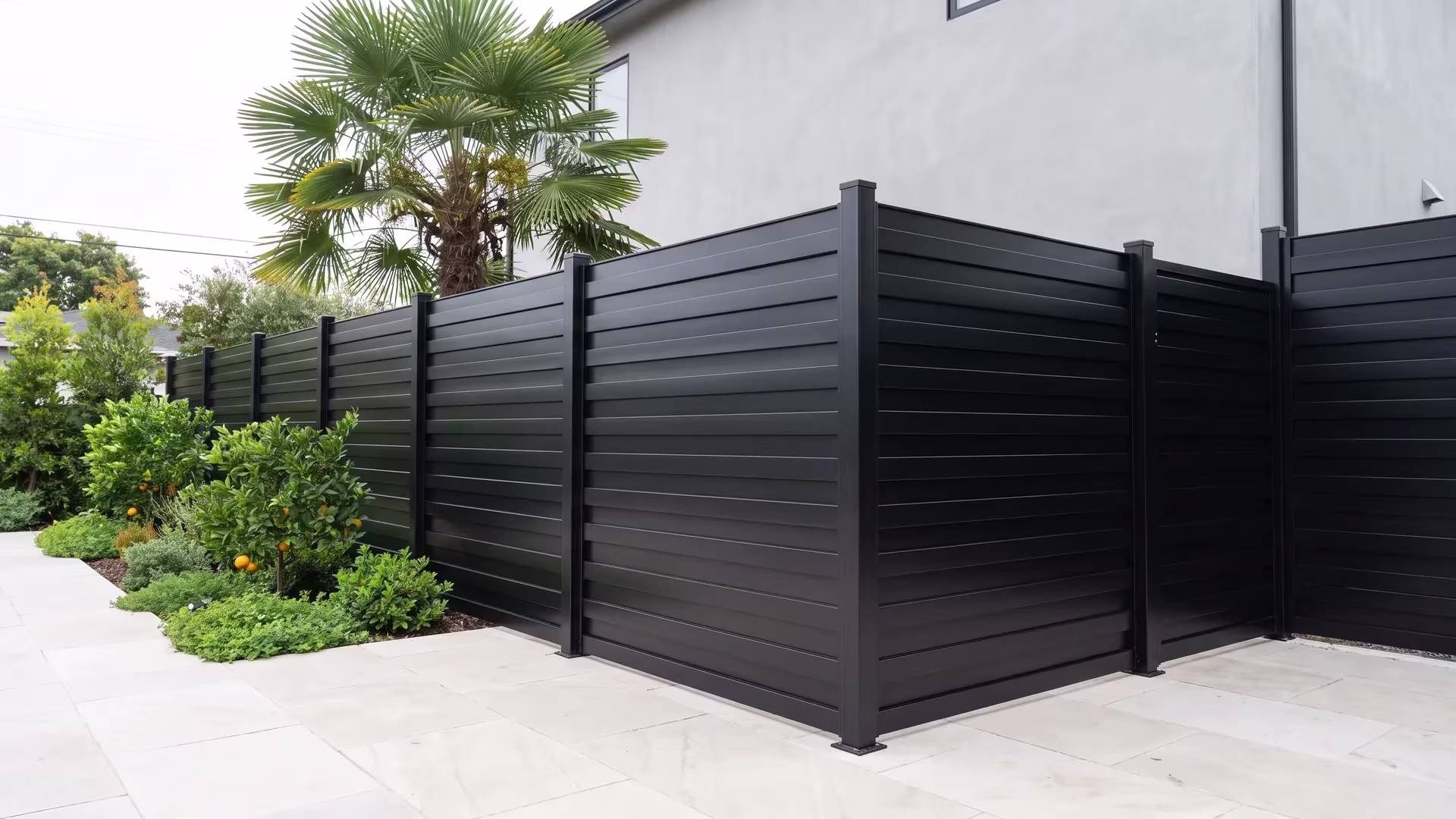 Pale stone paving runs past an aluminum horizontal privacy shadowbox fence in this urban backyard, finished in Black