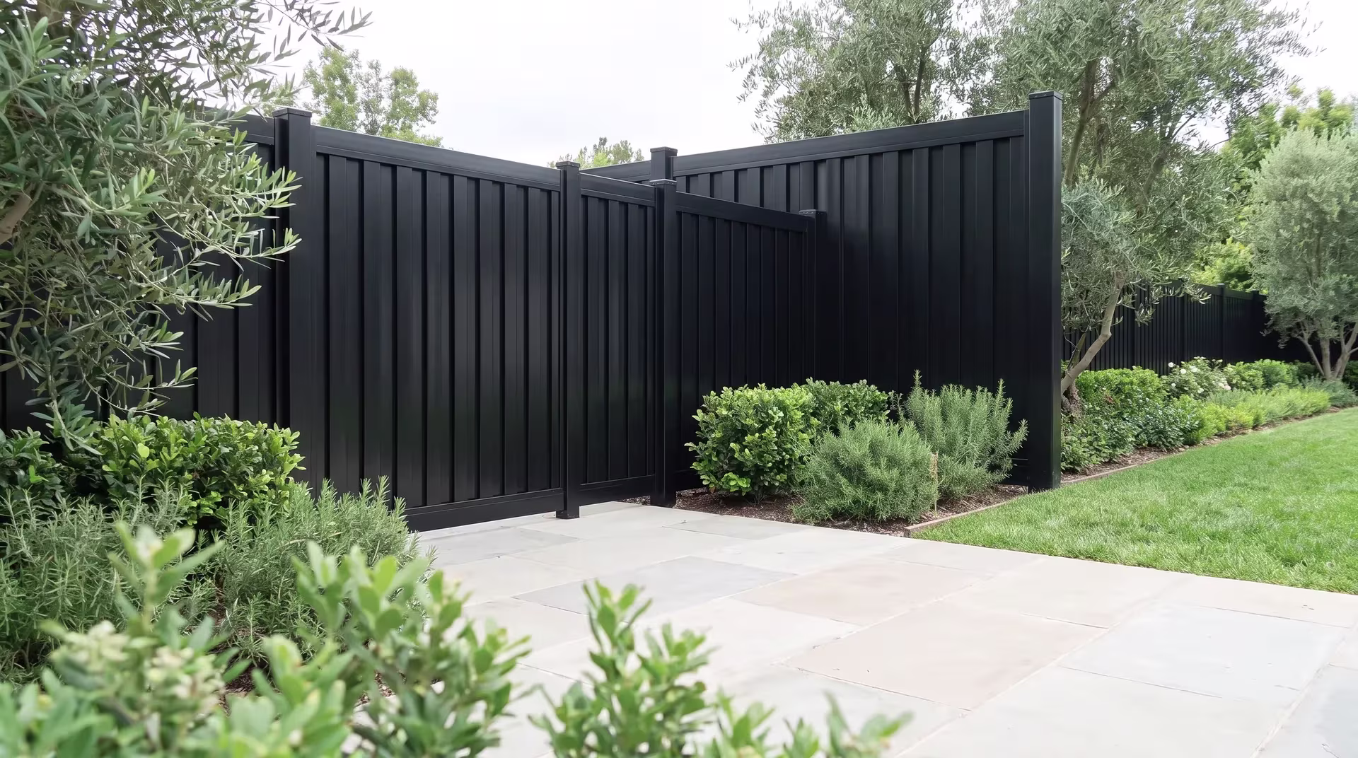 Olive trees and pittosporum flank this aluminum vertical privacy shadowbox fence in a suburban backyard, in Black