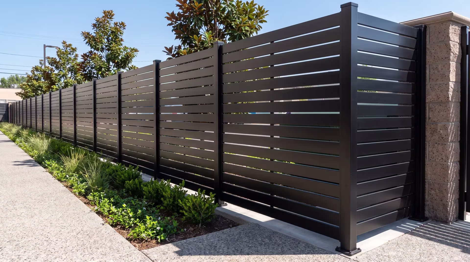 A masonry column anchors the Black aluminum semi privacy fence along a grocery market's planted boundary