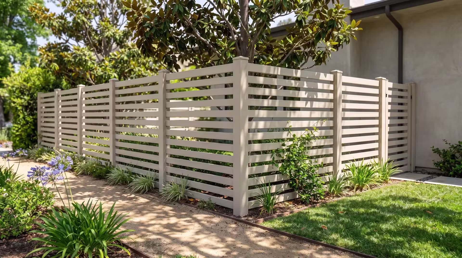 Decomposed granite paths edged in steel run beside a Tan horizontal picket vinyl fence near magnolia and jasmine