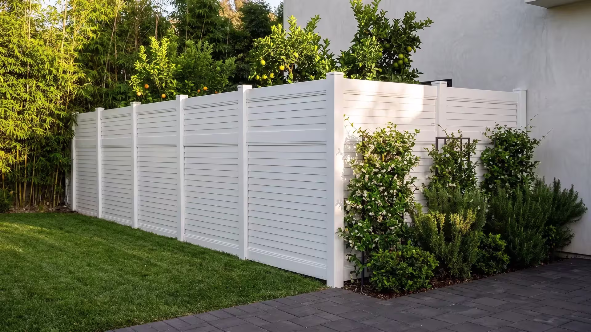 Bamboo and citrus planting screen a paved patio behind this White vinyl horizontal privacy fence