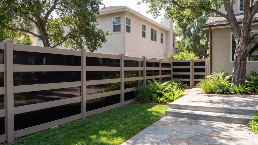 Ferns and lomandra soften poured concrete retaining edges beside a Clay vinyl privacy fence with acrylic