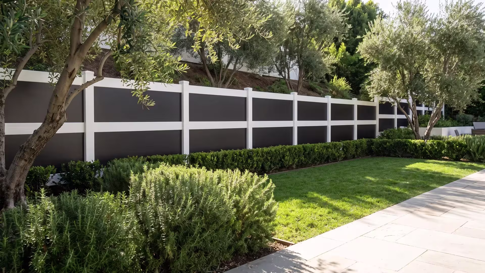 White vinyl privacy fence with acrylic set on pale stone paving among mature olive trees