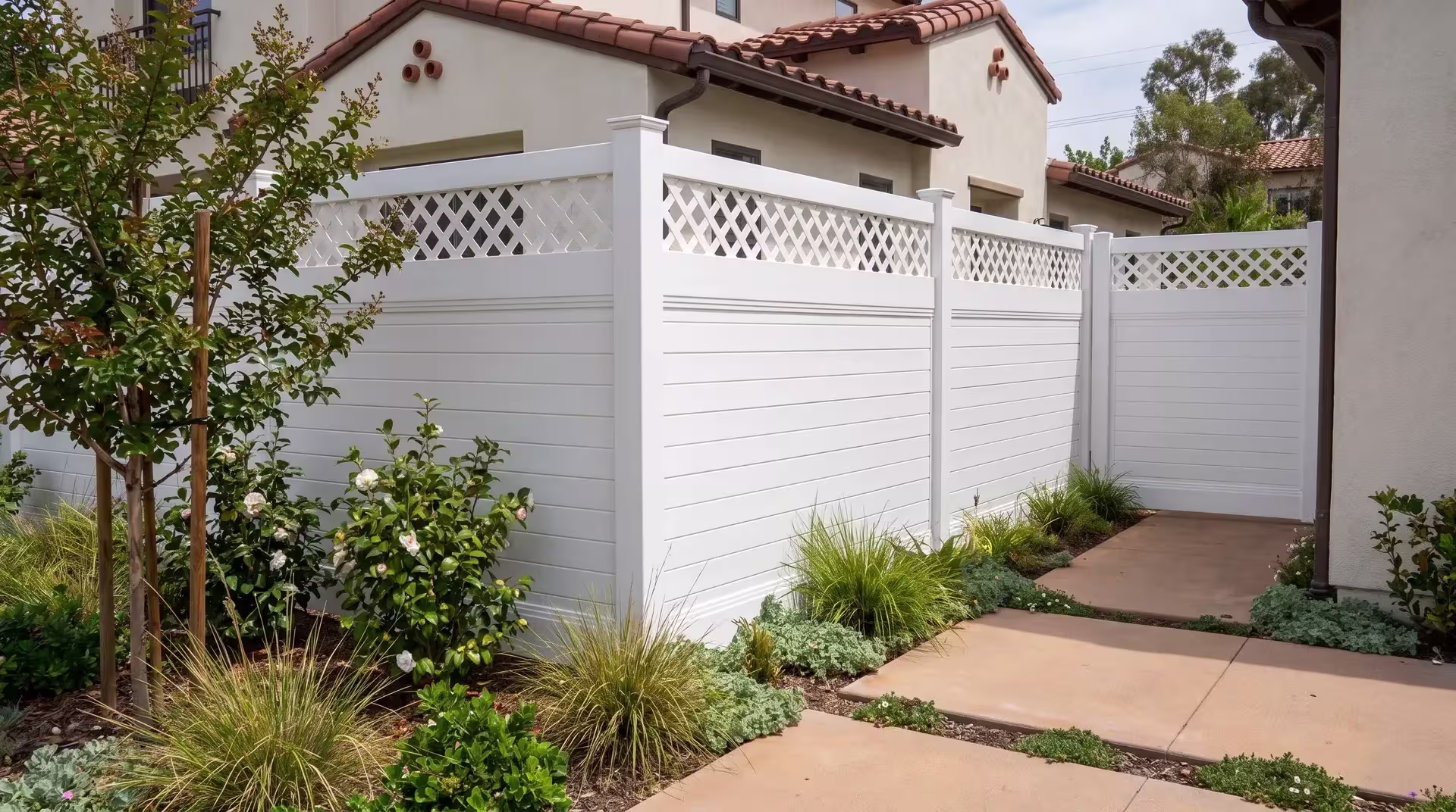 White vinyl horizontal privacy fence faces warm concrete pavers with narrow planted joints at a Mediterranean-style home