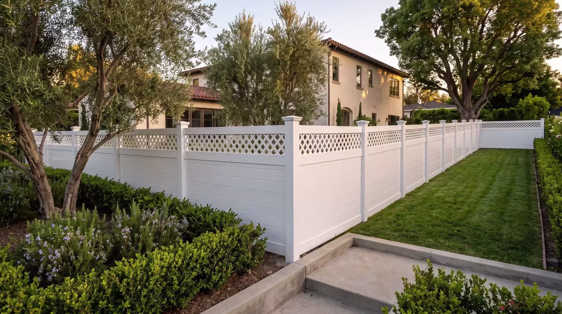Olive trees and pittosporum rise behind this White vinyl horizontal privacy fence at a Mediterranean-style home