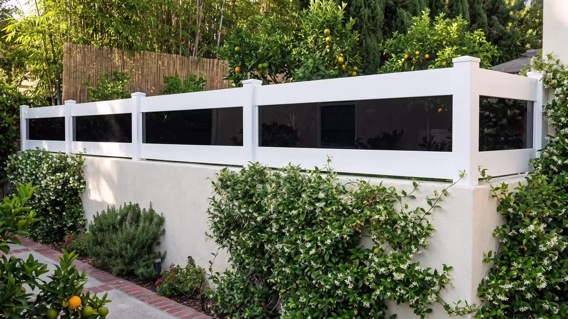 White vinyl wall topper with acrylic added atop a stuccoed garden wall for more privacy beside a brick path