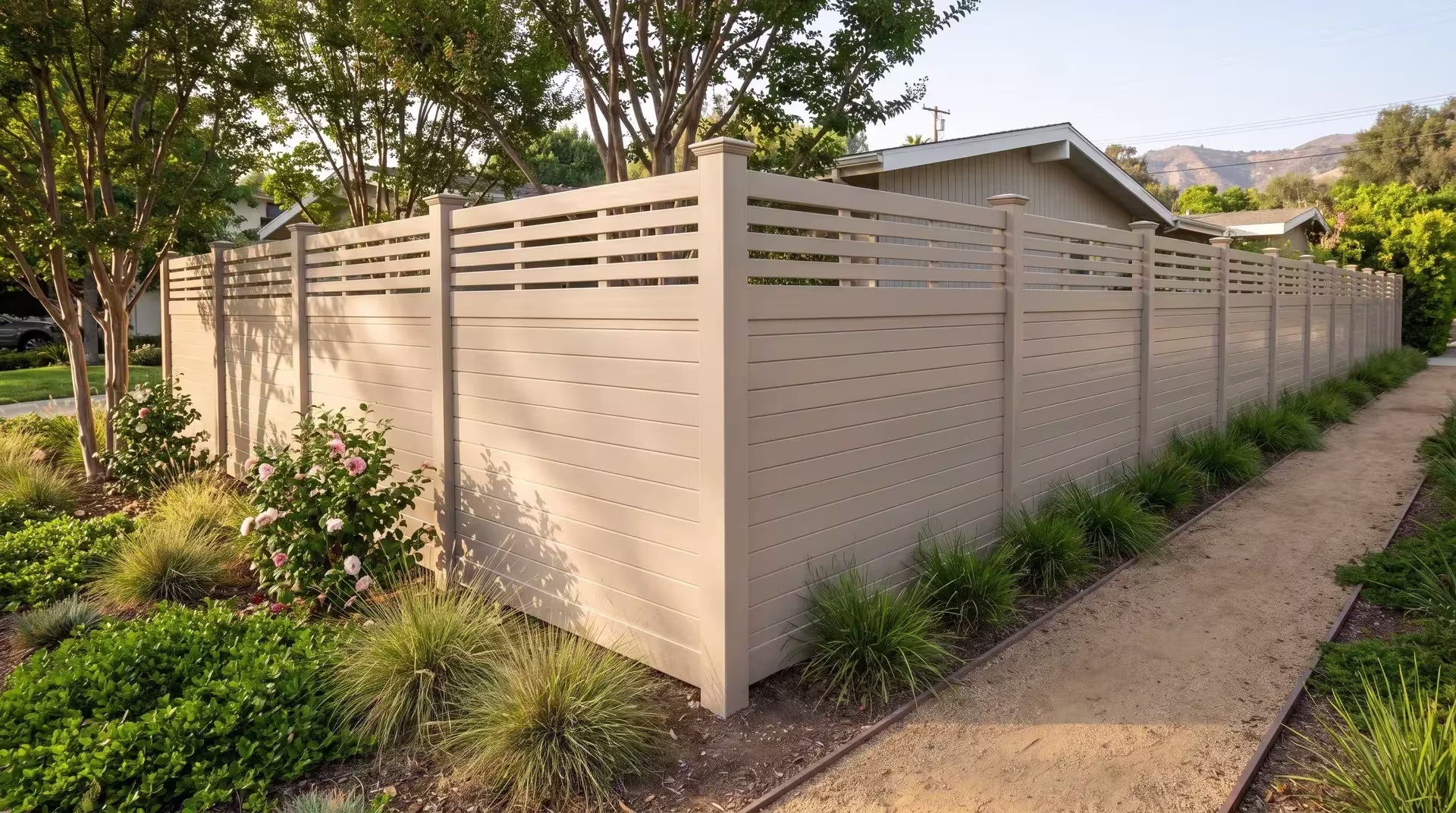Tan vinyl horizontal privacy fence frames a planted corner of crepe myrtle and camellias with a picket top