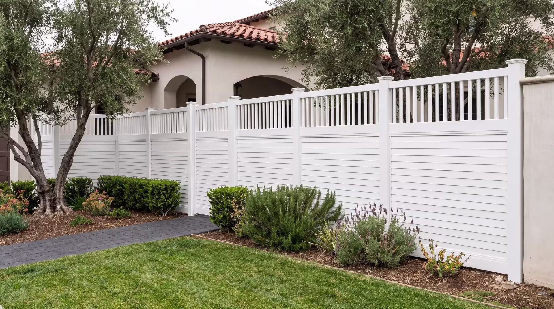 A Mediterranean style home rises beside a White vinyl privacy fence, horizontal panels capped with vertical pickets