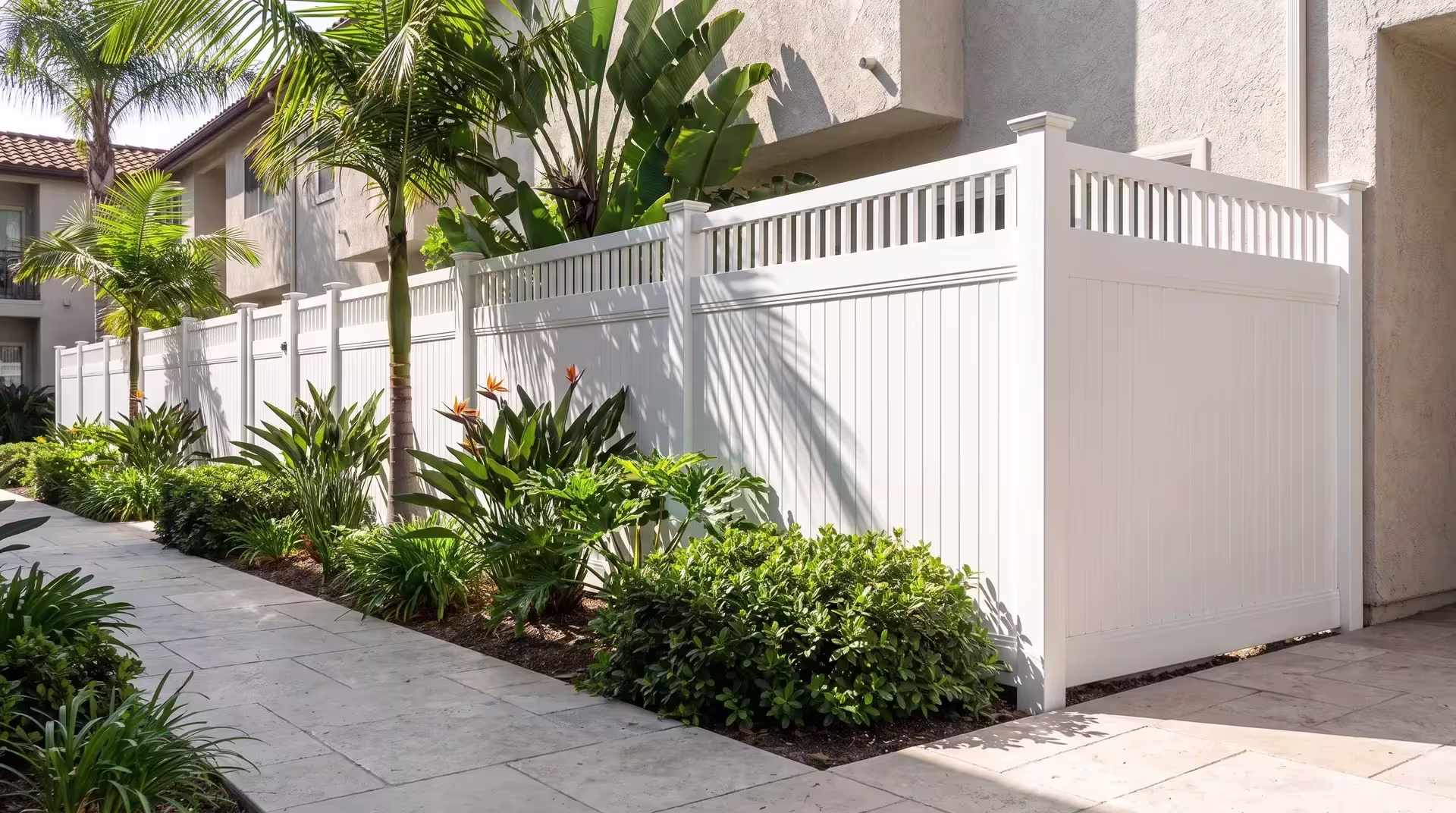 White vinyl fence wraps a courtyard beneath tall queen palms, picket-topped above its vertical privacy boards