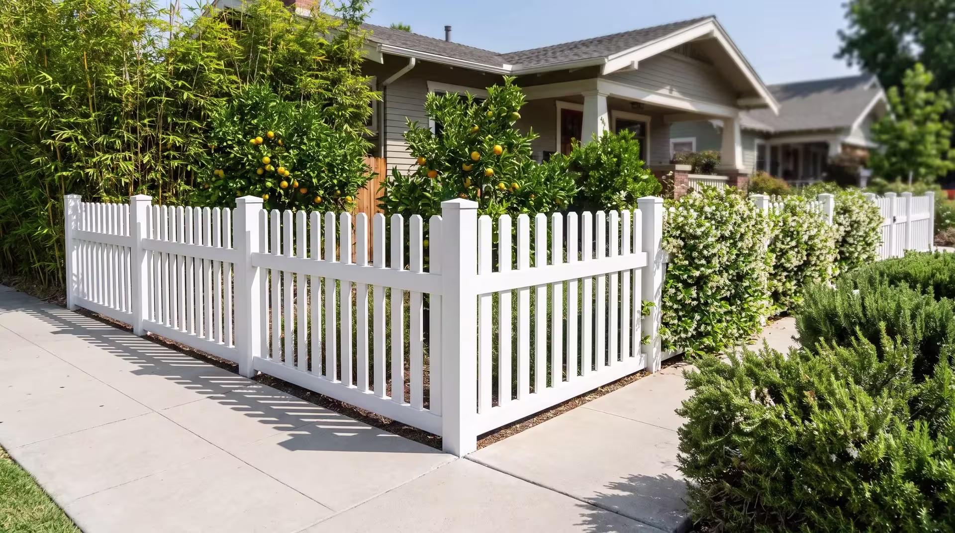 White vinyl straight picket fence turning a corner above a broom-finished concrete walk