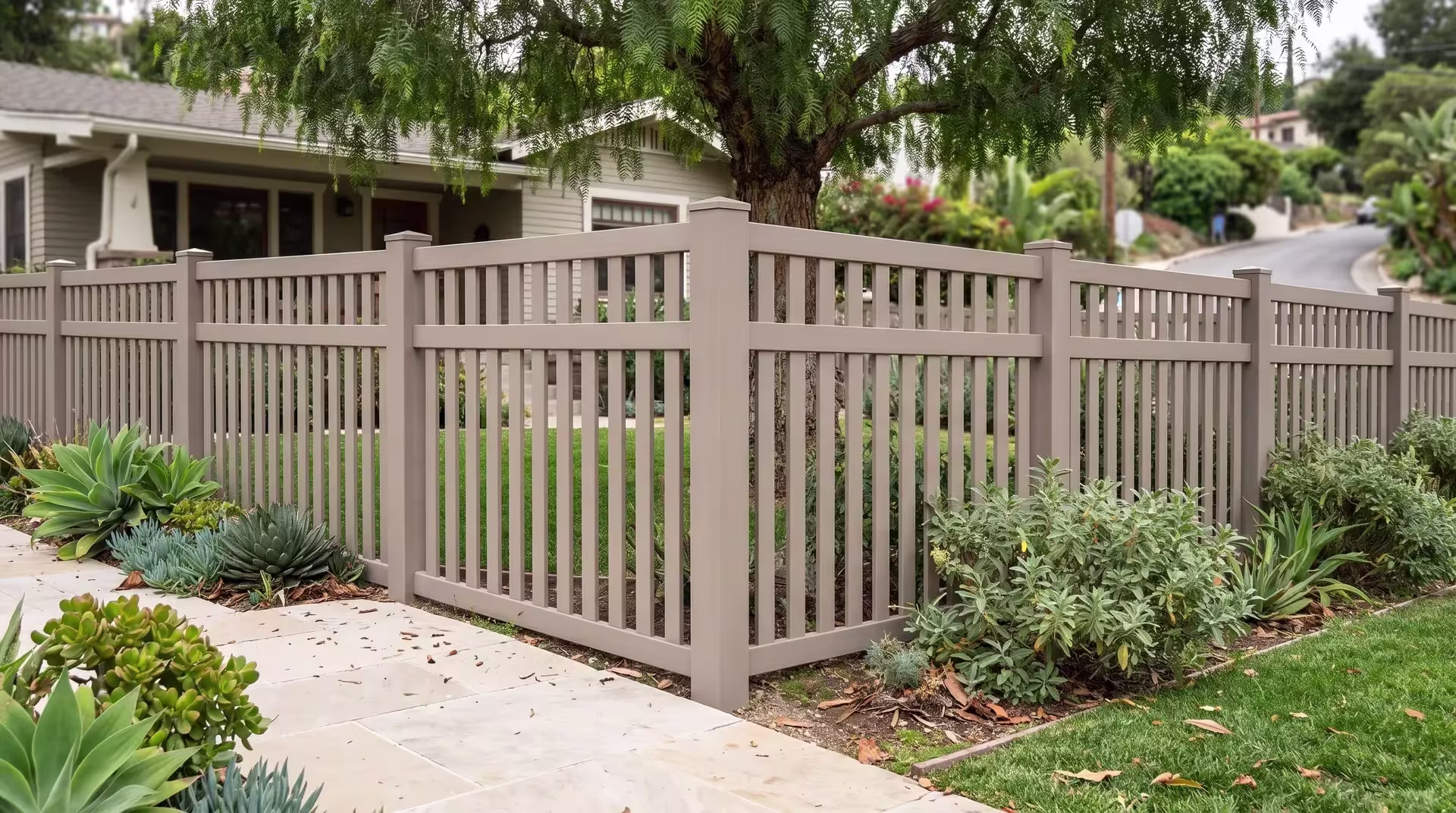 Clay vinyl picket fence turning the corner of a hillside lot edged in pale stone paving, closed top vertical boards