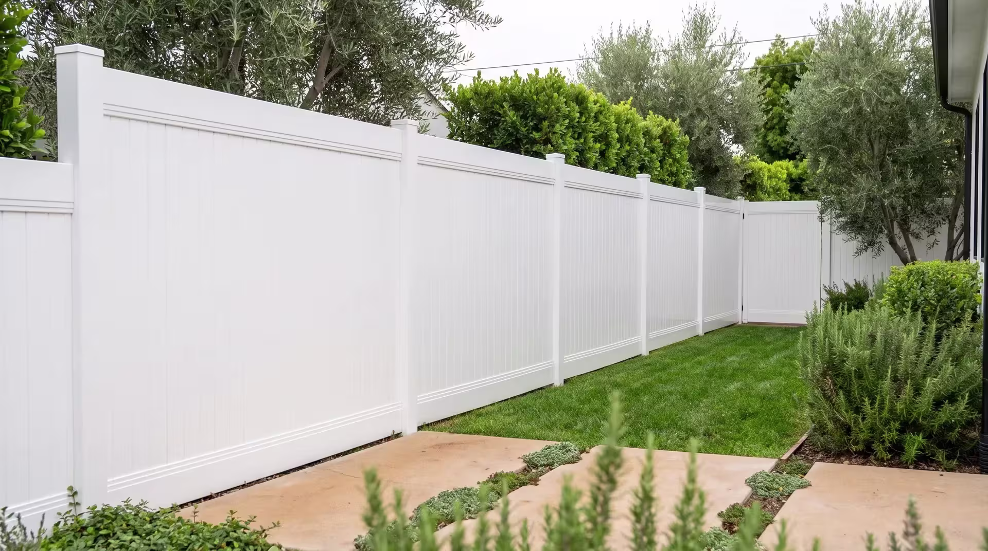Mature olive trees shade the concrete pavers a White vinyl privacy fence borders