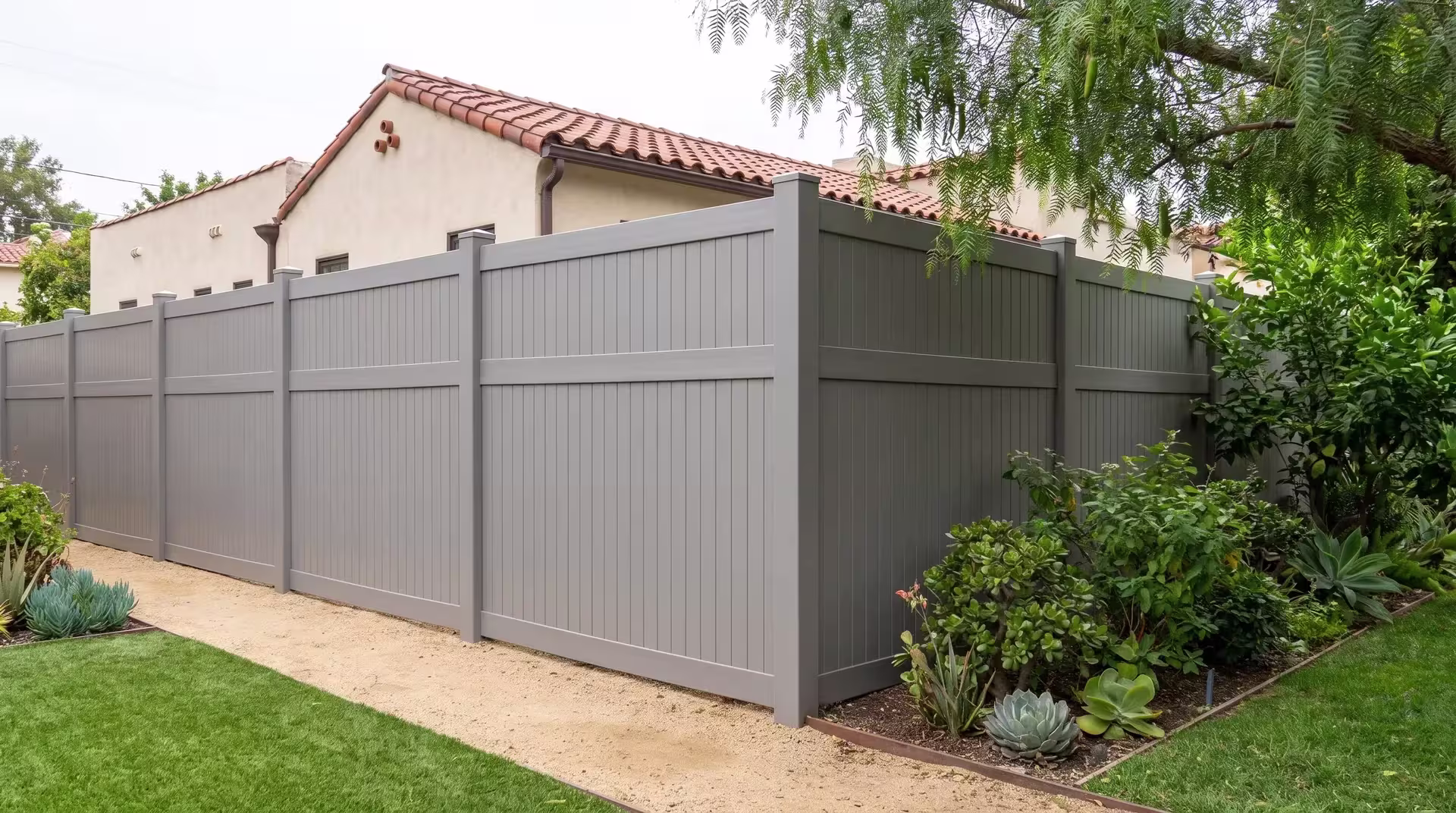 Slate Gray vinyl vertical privacy fencing closes a compact backyard beside a Mediterranean-style home and pepper tree