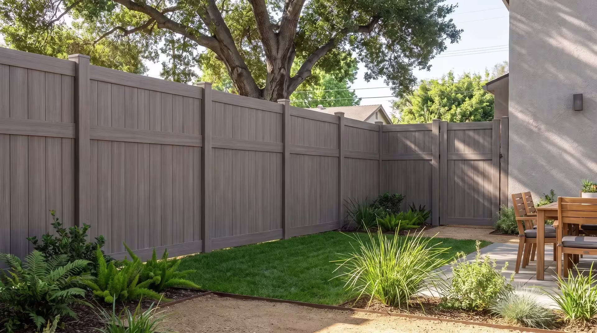 Coast live oak shade falls over this Weathered Blend vinyl fence, its vertical privacy boards beside a duplex terrace