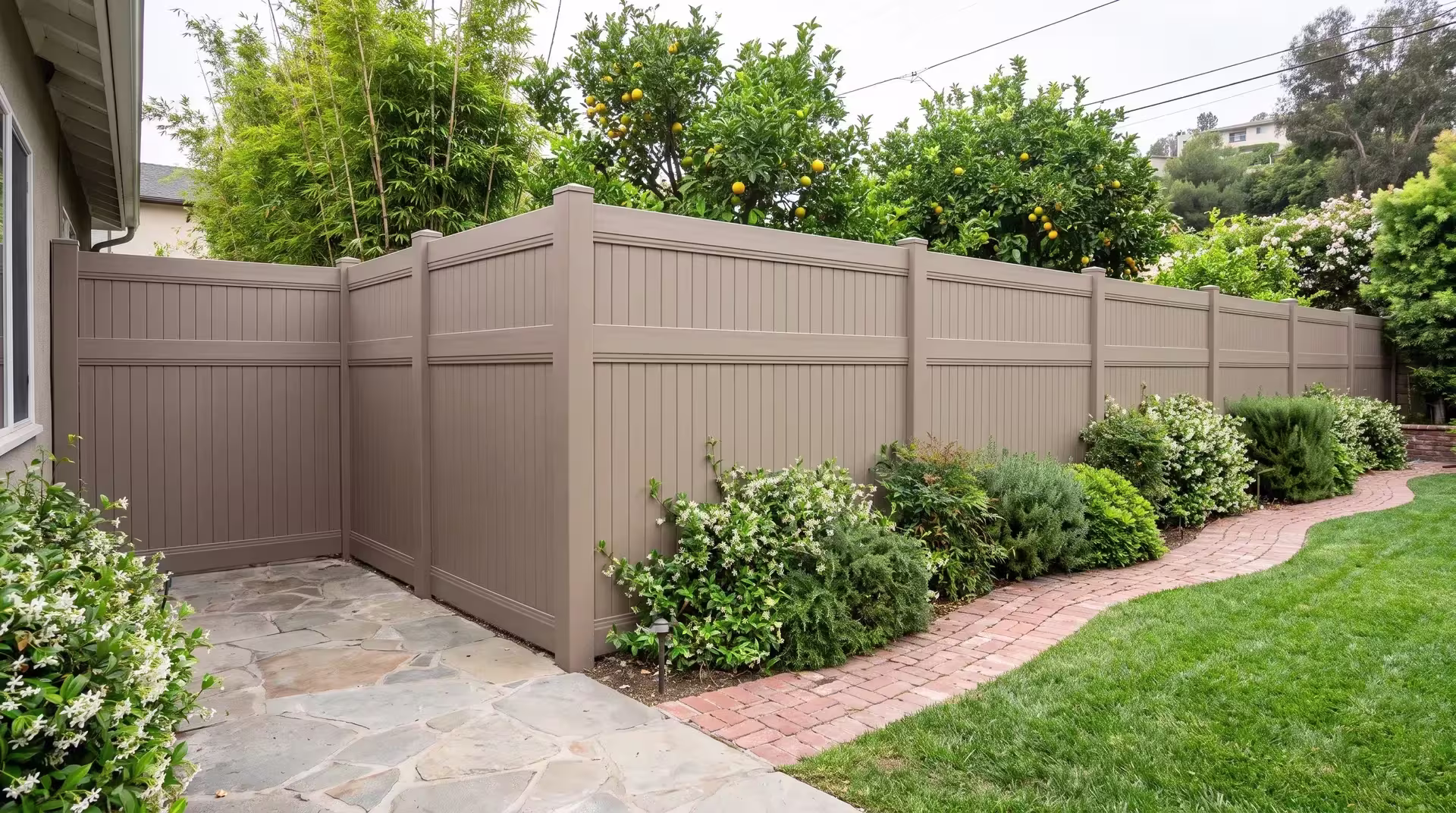 A brick-edged garden path runs beside Clay vinyl vertical privacy fencing and a bamboo screen at this hillside home