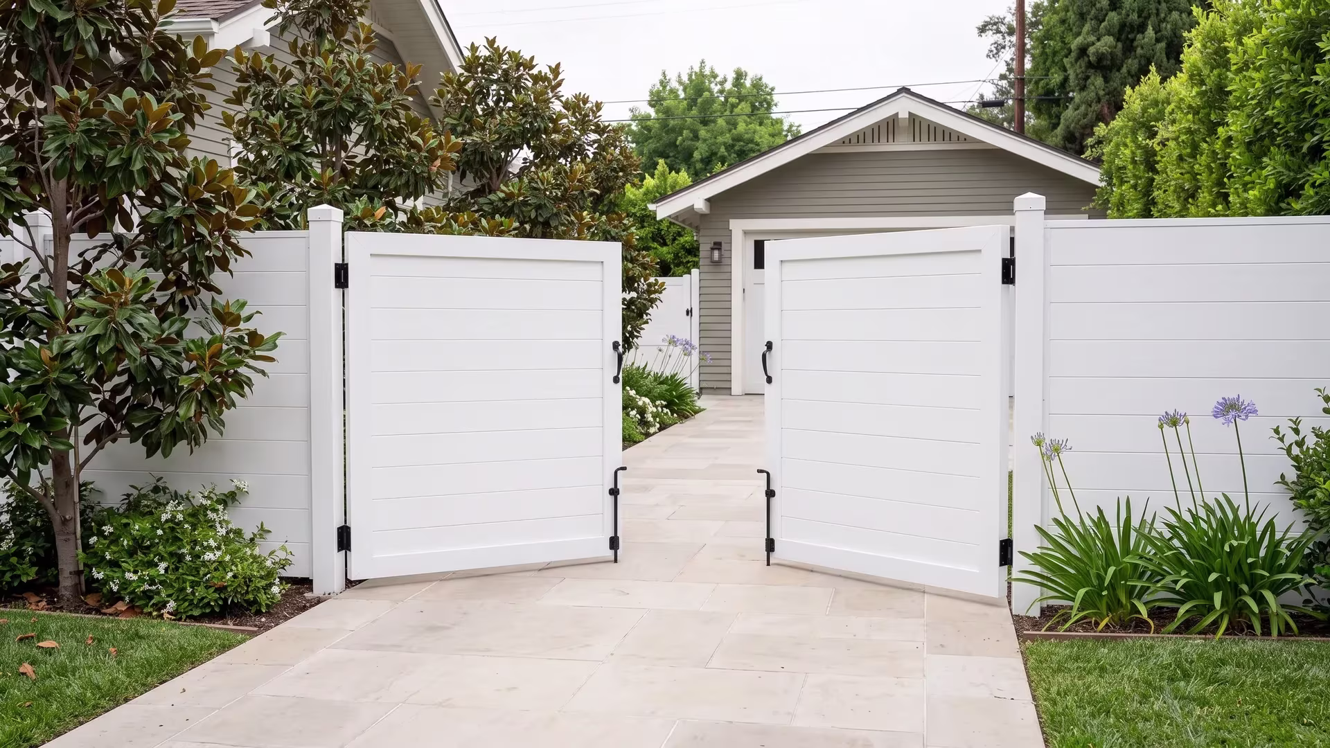 White double opening aluminum gate closed for full privacy, leading a side drive toward a detached rear garage