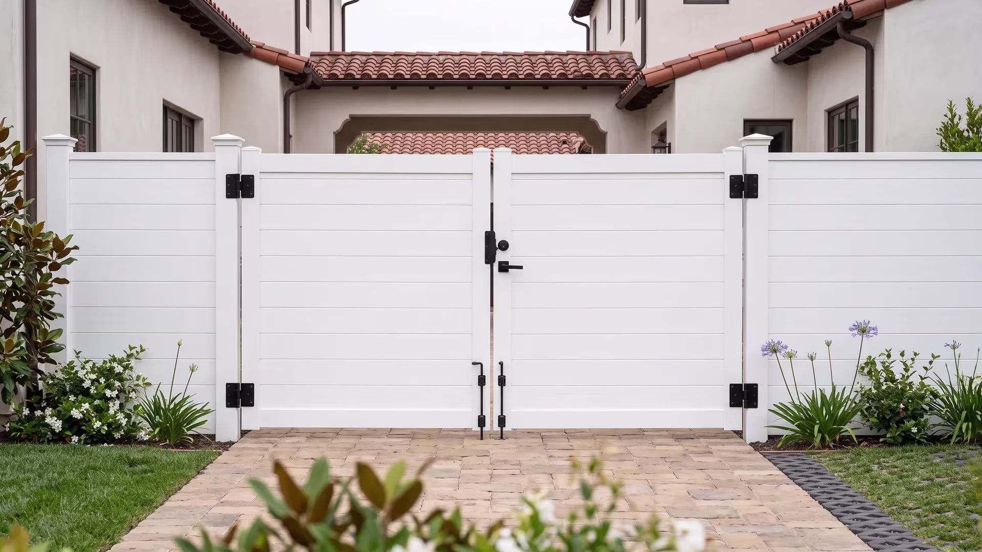 Full privacy aluminum driveway gate in White, spanning a stone-paved drive outside a Mediterranean courtyard
