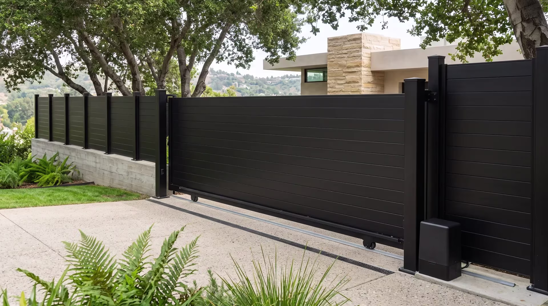 Black aluminum full privacy rolling gate closing off a parking terrace shaded by a coast live oak