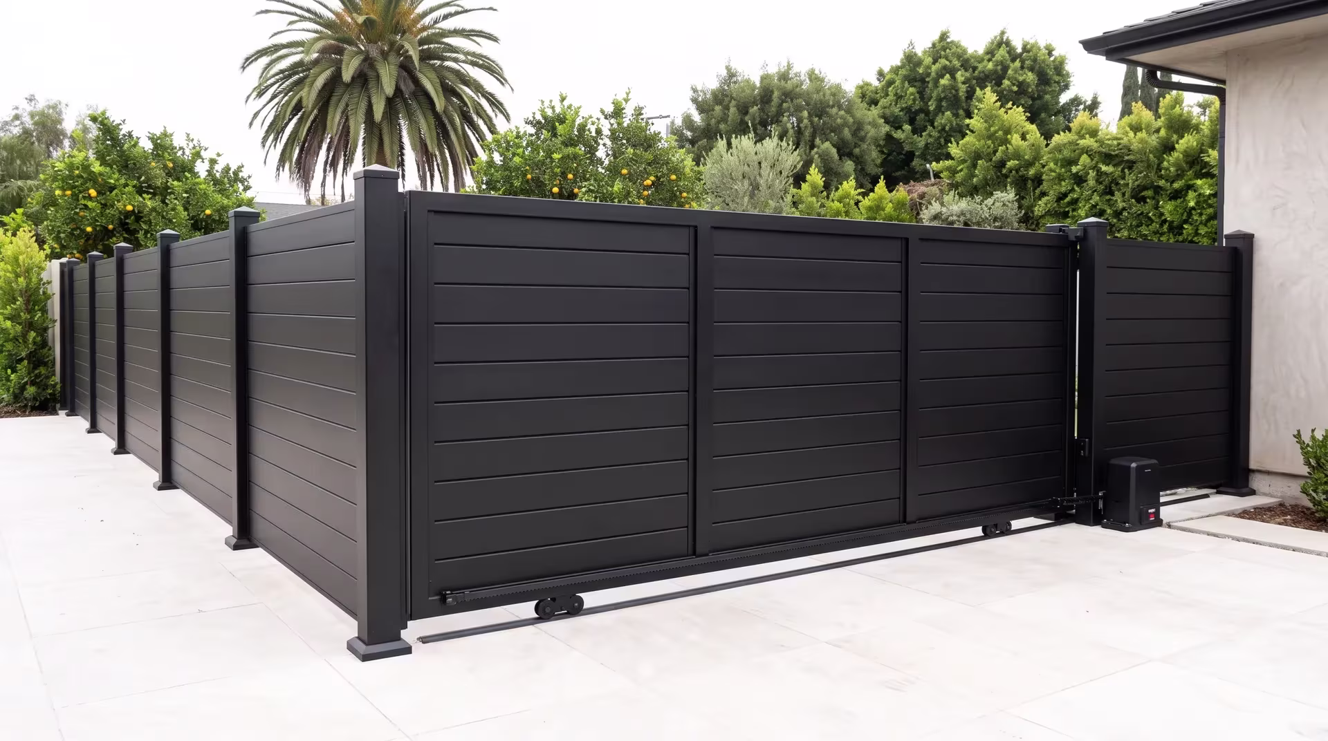 A Black full privacy aluminum rolling gate screens a driveway court beneath a tall fan palm