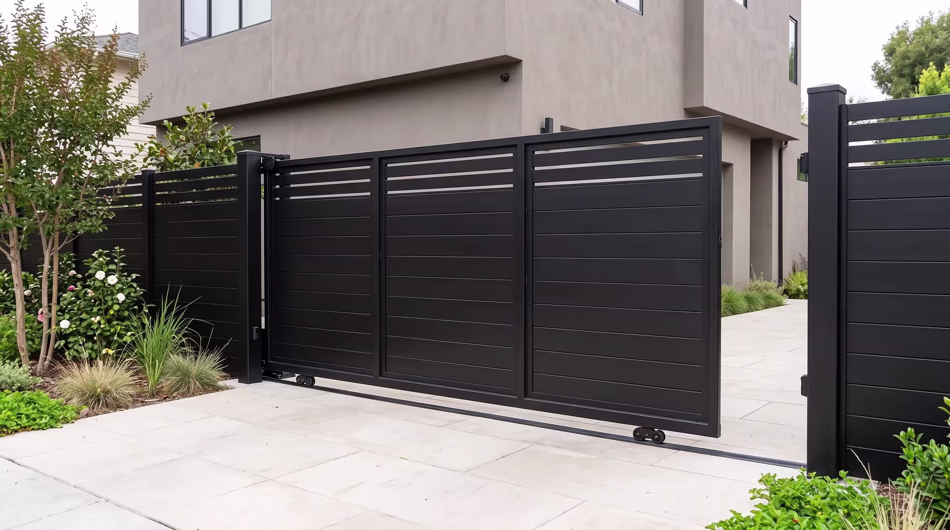 Black aluminum privacy hybrid rolling gate blending solid and open sections beside a stucco driveway facade