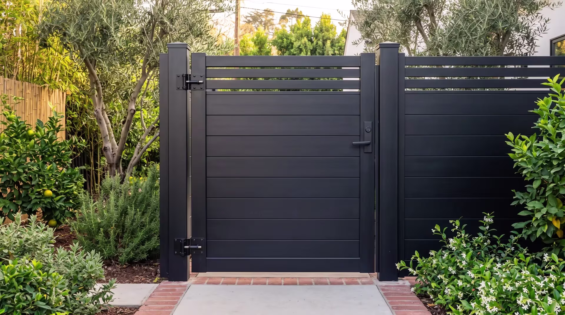 Black privacy hybrid aluminum single side gate set within a wide front drive framed by mature olive trees