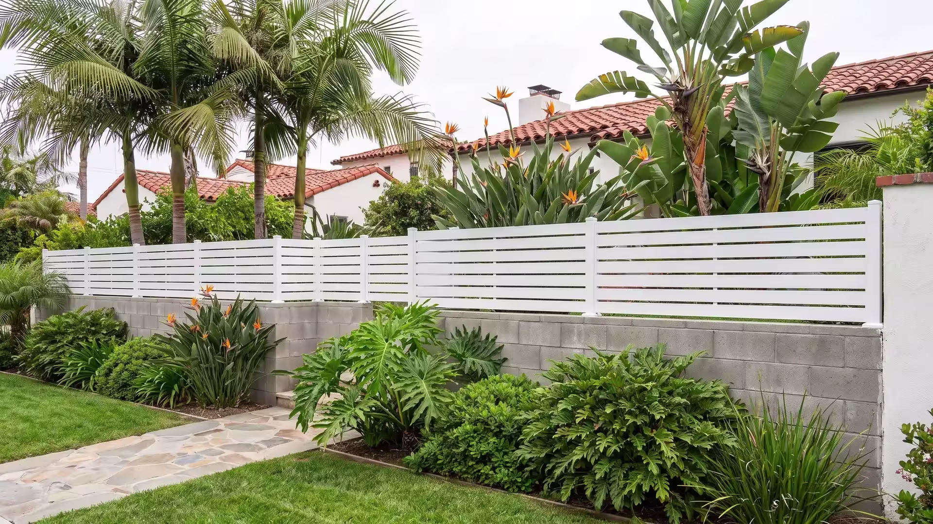 White aluminum semi privacy wall topper stops at a return corner on a split-face block wall near a Spanish Revival home